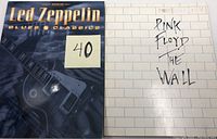 Photo of front covers of two guitar tab books: Led Zeppelin Blues Classics with dark blue cover and guitar image, and Pink Floyd The Wall with white brick wall cover and handwritten-style title.