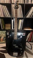 Silvertone black bass guitar displayed upright in front of amplifier, showing overall body shape and headstock