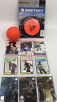 Full lot showing orange vinyl ball, sealed Gretzky branded vinyl puck packaging, and 9 hockey trading cards flat laid