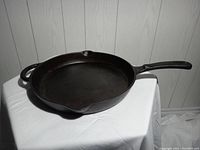 Side view of 12-inch cast iron frying pan showing long handle, smaller loop handle, and two pour spouts.