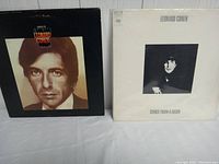 Front and back covers of the "Songs of Leonard Cohen" album showing Leonard Cohen's portrait on front and colorful artwork of a woman with flames on back.