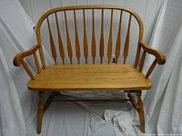Front view of the oak wooden bench showing smooth seat, curved armrests and spindle backrest