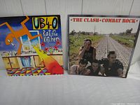 Front covers of The Clash 'Combat Rock' and UB40 'Rat in the Kitchen' albums showing band photo and colorful artwork respectively.