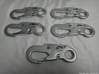 Top-down view of five identical metal snap hooks arranged on a white surface.