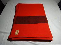 Folded pure wool blanket in bright orange with single dark brown stripe and Highlander Gordon Mackay label visible