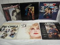 Six vinyl soundtrack albums displayed on white cloth surface, front covers showing movie titles and images from Vision Quest, Footloose, Top Gun, The Big Chill, Who's That Girl, and Wall Street.