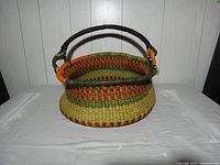 Front view of round Bolga basket showing the curved leather-covered handle and orange and green woven accents.