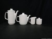 Front view of the Johnson Brothers Athena coffee pot, tea pot, creamer, and sugar bowl, all white ceramic with ridged vertical texture.