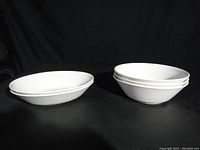 Two stacks of white ceramic serving bowls, two oval bowls on the left and three round bowls on the right with textured rib pattern on rim edges.