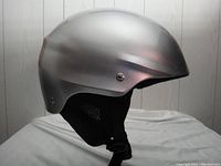 Side view of silver unisex ski helmet showing smooth matte finish and padded ear section with adjustable chin strap.