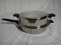 Photo of the stainless steel egg poacher stacked closed with dual lids, showing black plastic handles on sides and one long handle.