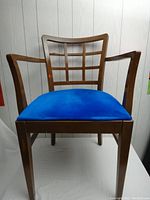 Front-facing photo showing the wooden chair's square grid backrest and blue velvet seat.