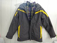 Front and hood view of black ski jacket with yellow accents and visible inner jacket with plaid pattern showing at collar.