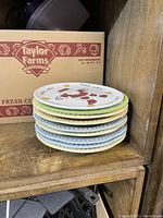Stack of nine ceramic and glass plates arranged on wooden shelf, showing multicolored patterns and various plate designs.