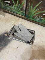 All items in the lot arranged together on the floor, including three metal rectangular baking pans stacked and gray quilted fabric oven mitts laid on top.