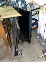 Side view showing two flatscreen televisions standing on the floor side by side, power cords visible, no remotes shown.