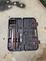 Photo of complete grill tool kit laid out in molded plastic case on a concrete surface.