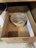 Small metal napkin holder inside small woven basket in cardboard box.