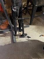 Black small air pump with hose and nozzle visible, set on concrete floor with other workshop items in background.