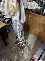 Vintage upright electric vacuum cleaner with a gray cloth bag and a power cord wrapped around the handle, standing on a concrete floor in a cluttered indoor space.