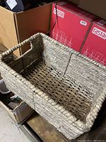 Close-up photo of one small rectangular woven basket made from thick natural fibers with cutout handles.