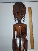 Front view showing the human figure with detailed headdress, facial features, and arm holding an object with ruler for scale.