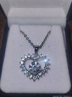Silver plated heart-shaped pendant necklace with central large synthetic stone surrounded by smaller stones, displayed in a jewelry box.