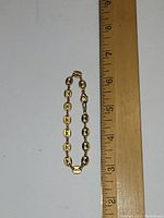 Gold tone bracelet displayed next to a ruler for size reference showing approximately 7.75 inches length.