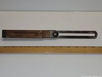 Antique adjustable compass square made of wood and metal laid next to a ruler for size reference.