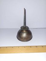 Oil can front view showing embossed Ford logo and tarnished metal surface with ruler for scale.