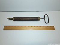 Full view of antique brass grease tool plunger with T-shaped handle and tapered nozzle, measuring about 14 inches with a ruler beside it.
