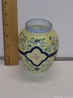 Full front side of the vase with ruler showing size, hand painted decorative floral design on opaque milk glass.