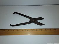 Photo of antique hand sheers with roughly 9 inch length shown next to a ruler, darkened metal surface, pivot joint visible.