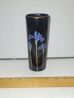 Front view of the black vase with blue iris floral design and gold rim placed next to a ruler showing approximately 6 inches in height.
