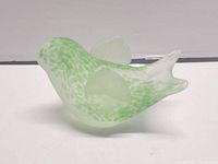 Side angle showing the bird's smooth rounded body, speckled green design, and frosted wings on a flat white surface.