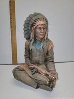 Side view of chalkware sculpture showing Native American chief sitting cross-legged with pipe, detailed headdress and clothing.