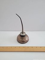 Front view of vintage oil can next to a ruler for size reference, approx. 9 inches tall and 3 inches wide.