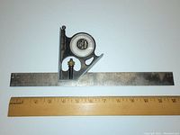 Photo showing the full length of the 12-inch metal ruler with the black cast head featuring a round center meter on top, placed next to a wooden ruler for scale.