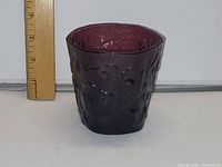 Side view of amethyst glass cup showing height compared to ruler, approximately 4 inches tall. Textured embossed design visible on surface.