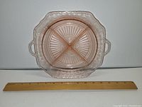 Pink Depression glass dish with four sections visible, two handles on sides, placed next to a ruler for size reference.