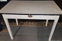 Front view of white kitchen table showing porcelain enamel top and wood base with drawer closed.