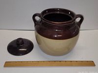 Pottery stoneware crock with lid and wooden ruler for scale, showing dark brown top and beige bottom.
