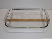 Top view of rectangular glass oven dish with a ruler inside showing 16 inch length, clear glass with scratches visible.