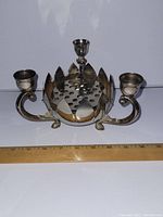 Front view of silver plated candle holder centerpiece showing two side candle cups and perforated floral arrangement base with petal-shaped edges.