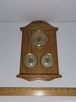 Front view of solid oak wall mount barometer showing three brass circular dials and a ruler for size reference