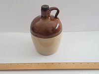 Full view of the tan and brown stoneware crock jug with handle and narrow neck, showing overall shape and design.