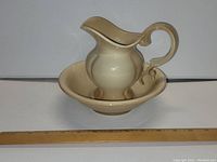 Image of the handmade ceramic pitcher placed inside the basin with a ruler for size reference, showing cream color and glossy finish.