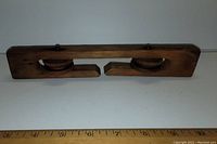 Top view showing the entire wooden pulley with two wheels and a ruler for scale.