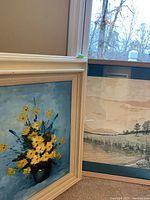 Photo showing the two framed artworks leaning against the wall: the floral oil painting and the lake landscape print