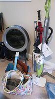 Items shown include a Bonaire fan, umbrellas in a ceramic umbrella stand, Smart Living steam mop with manual, and assorted bags on floor and blue metal chair.